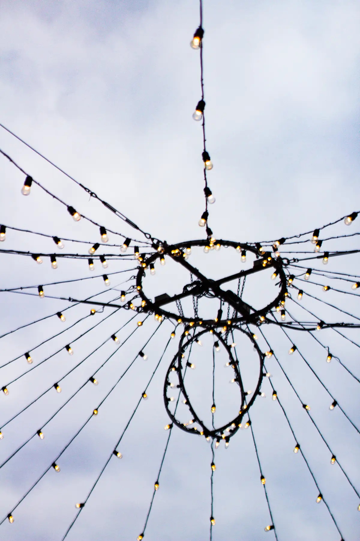 Strings of warm bulbs hung in a canopy over a pathway at the Toronto Christmas Market in the Distillery District, against an evening sky