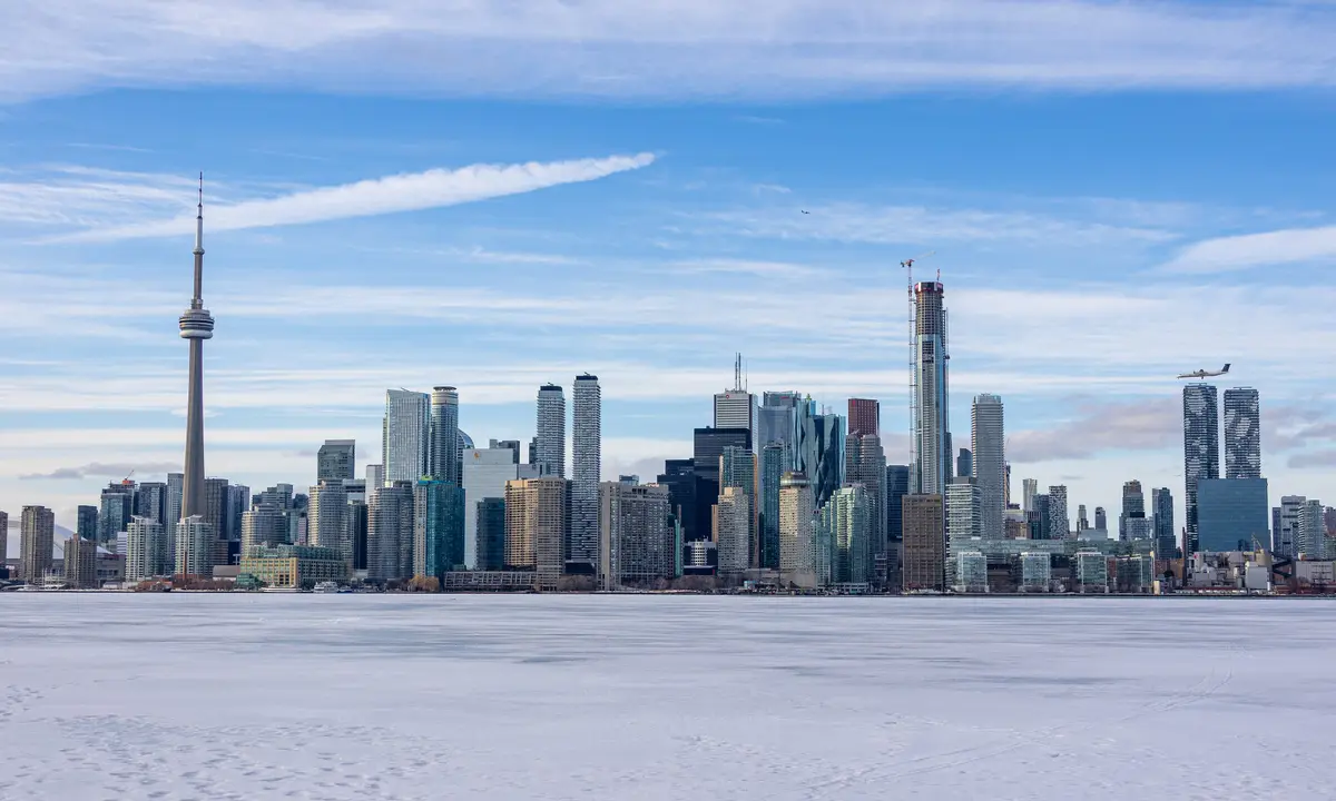 The Toronto skyline and CN Tower beyond a snow-covered frozen lake, seen from Snake Island on a bright winter day.